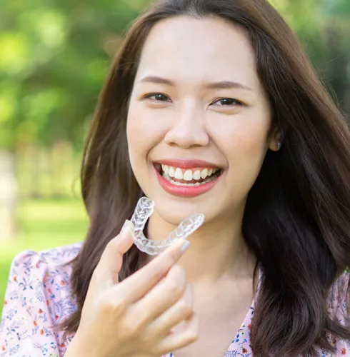 A woman smiling holding clear aligners